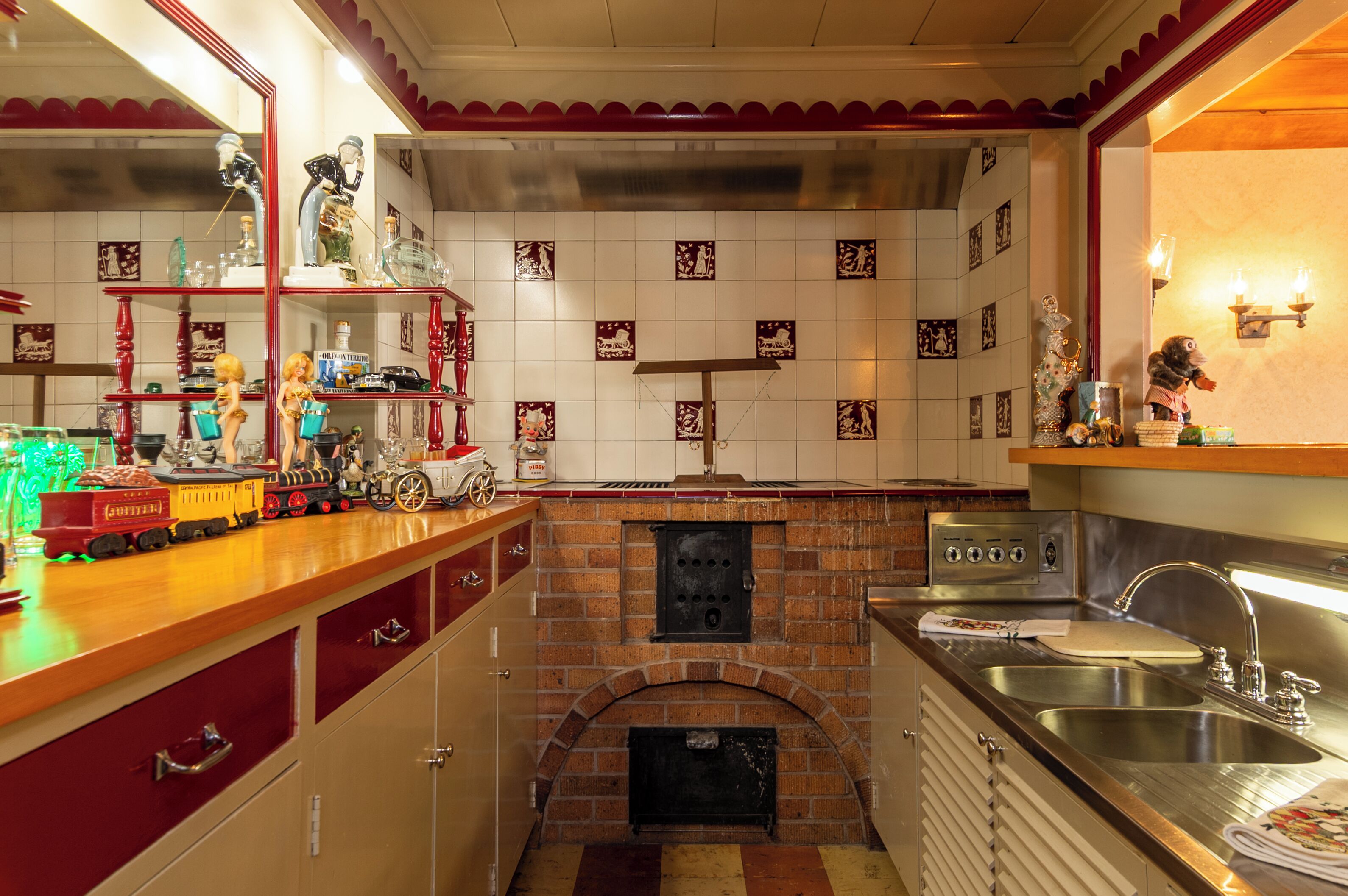 A kitchen with a brick oven, stainless steel sink, and a toy train display.