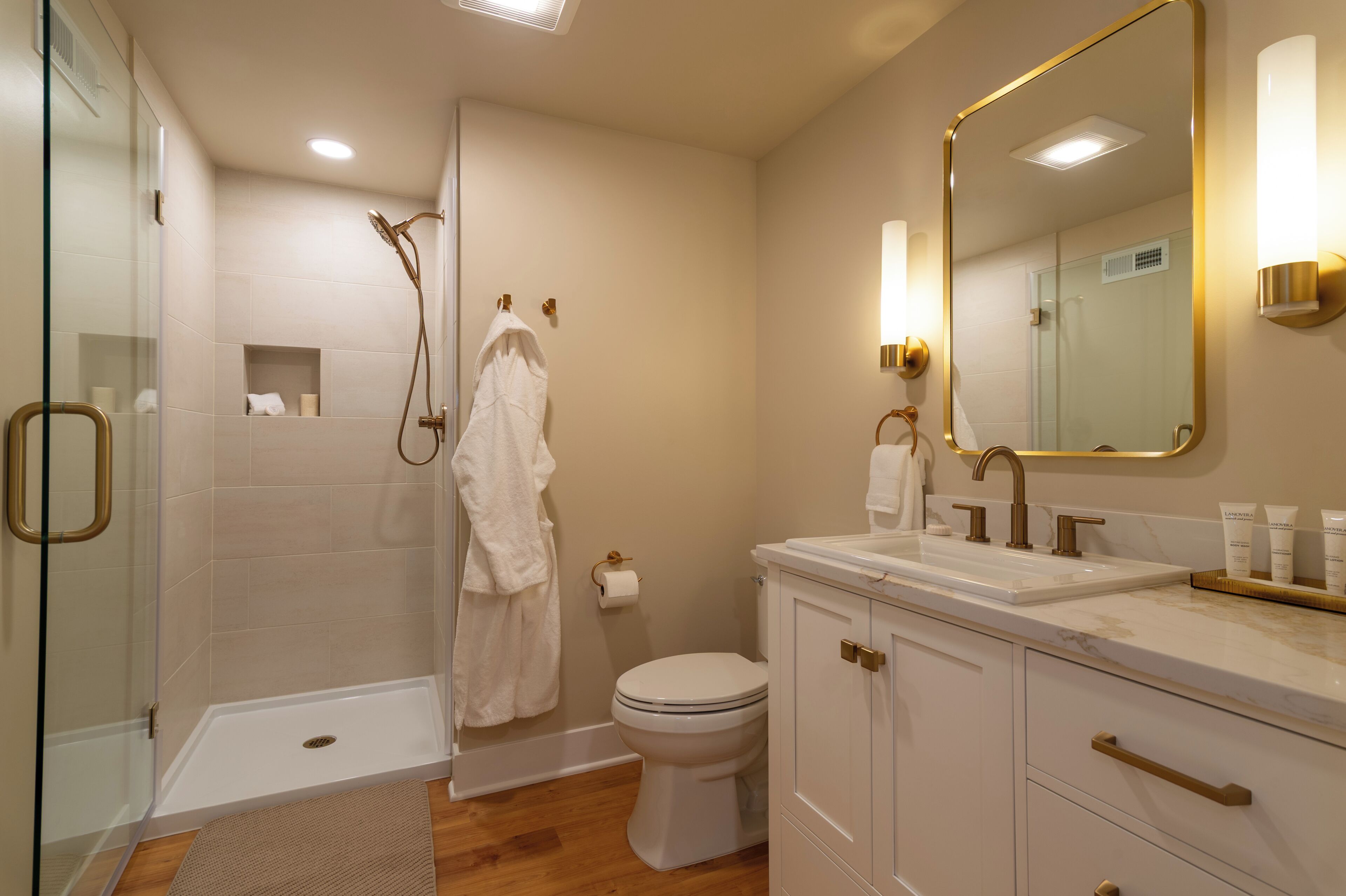 Une salle de bain avec une douche à parois de verre, des toilettes, un lavabo avec un miroir et un meuble-lavabo avec des placards.