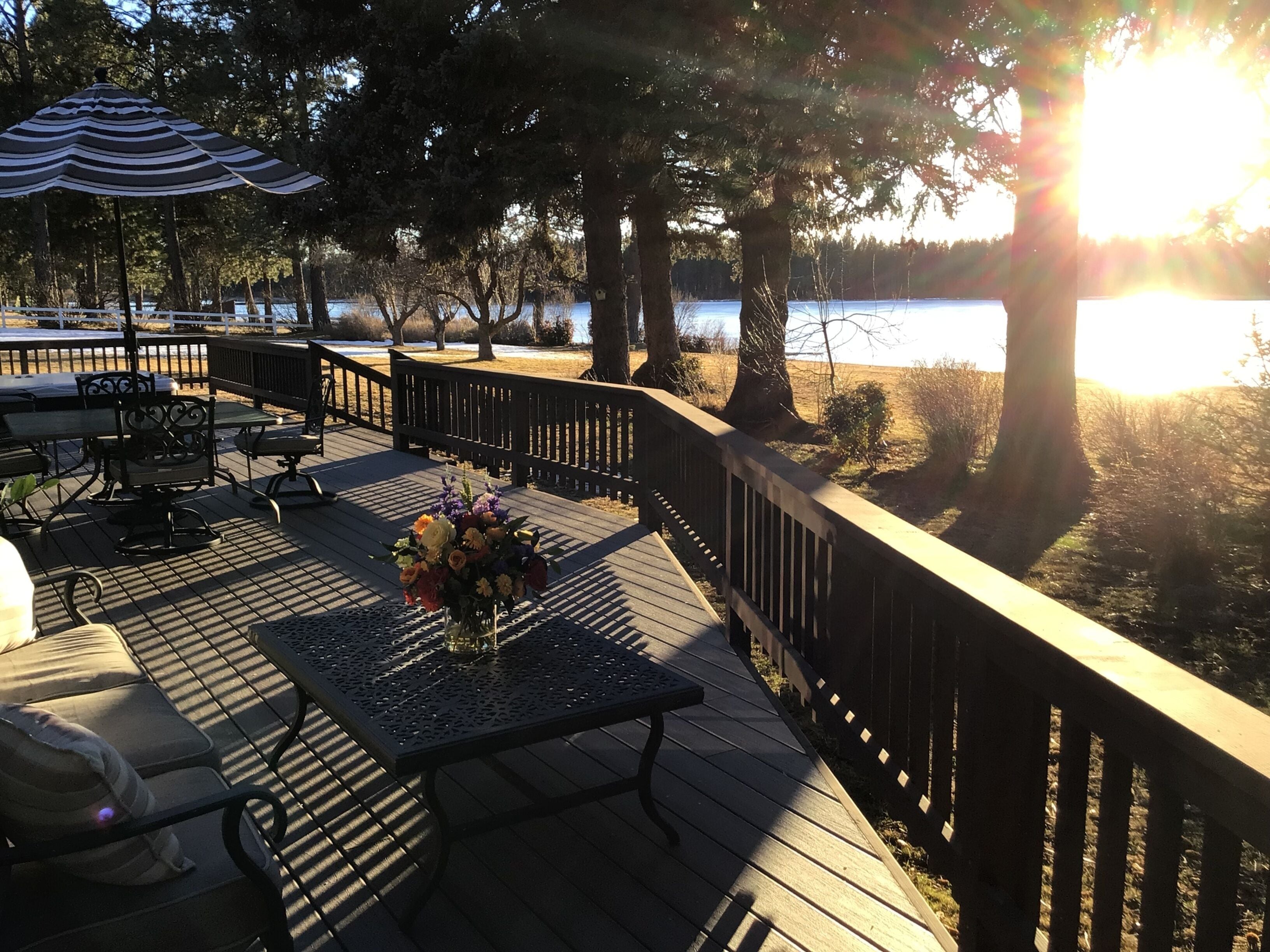 A wooden deck with outdoor furniture, a table with a vase of flowers, and a view of a body of water.