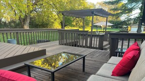 Una terraza de madera con mobiliario exterior, incluyendo un sofá y una mesa, y una estructura de pérgola.