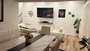 Una sala de estar moderna con comedor, televisor montado en la pared y una escalera que sube a otro nivel.