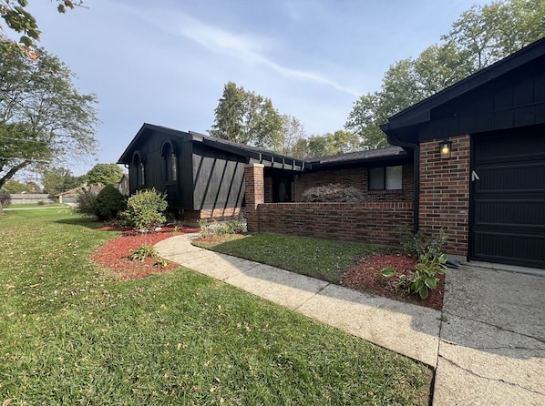Une maison moderne à deux étages, dotée d’une façade en briques, d’une porte de garage noire et d’une pelouse bien entretenue agrémentée de parterres de paillis rouge.