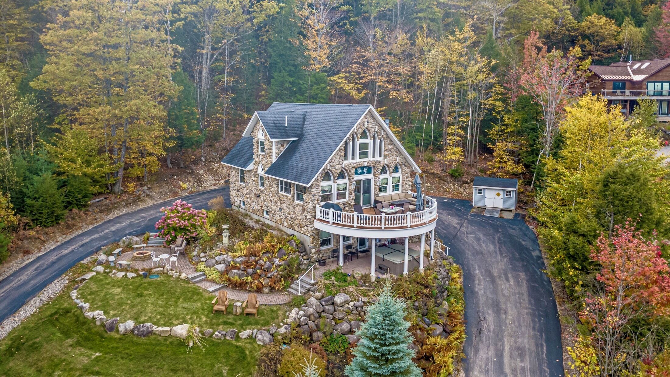 A stone house with a wrap-around porch, surrounded by a forested area.