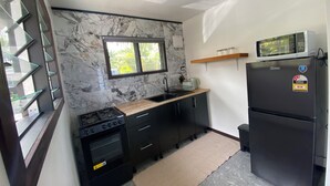A compact kitchen with a gas stove, oven, black refrigerator, and a microwave on top of the fridge. - Manta-Ray Beach Unit 2 (Rarotonga)