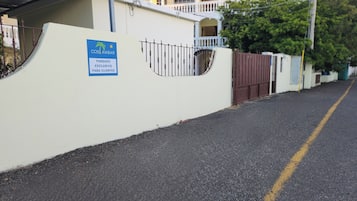 Une entrée fermée par un portail, sur laquelle on peut lire l’inscription « COSI LAMBAR, PARC DE STATIONNEMENT RÉSERVÉ AUX CLIENTS », et, au fond, un bâtiment à la façade blanche et au toit recouvert de tuiles rouges.