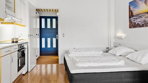 A modern hotel room with a kitchenette, a bed with white linens, a view of the sea, and a blue door. - Amazing apartment in Nexø with WiFi (Nexø)
