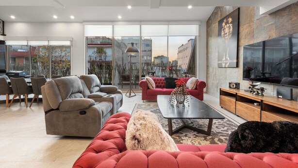 Ein modernes Wohnzimmer mit einem roten Sofa, grauen Sesseln und einem Fernseher.