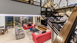 Ein modernes Wohnzimmer mit einem roten Sofa, einem grauen Sofa und einem Couchtisch. Eine Treppe mit Metallgeländer führt zu einer oberen Ebene.
