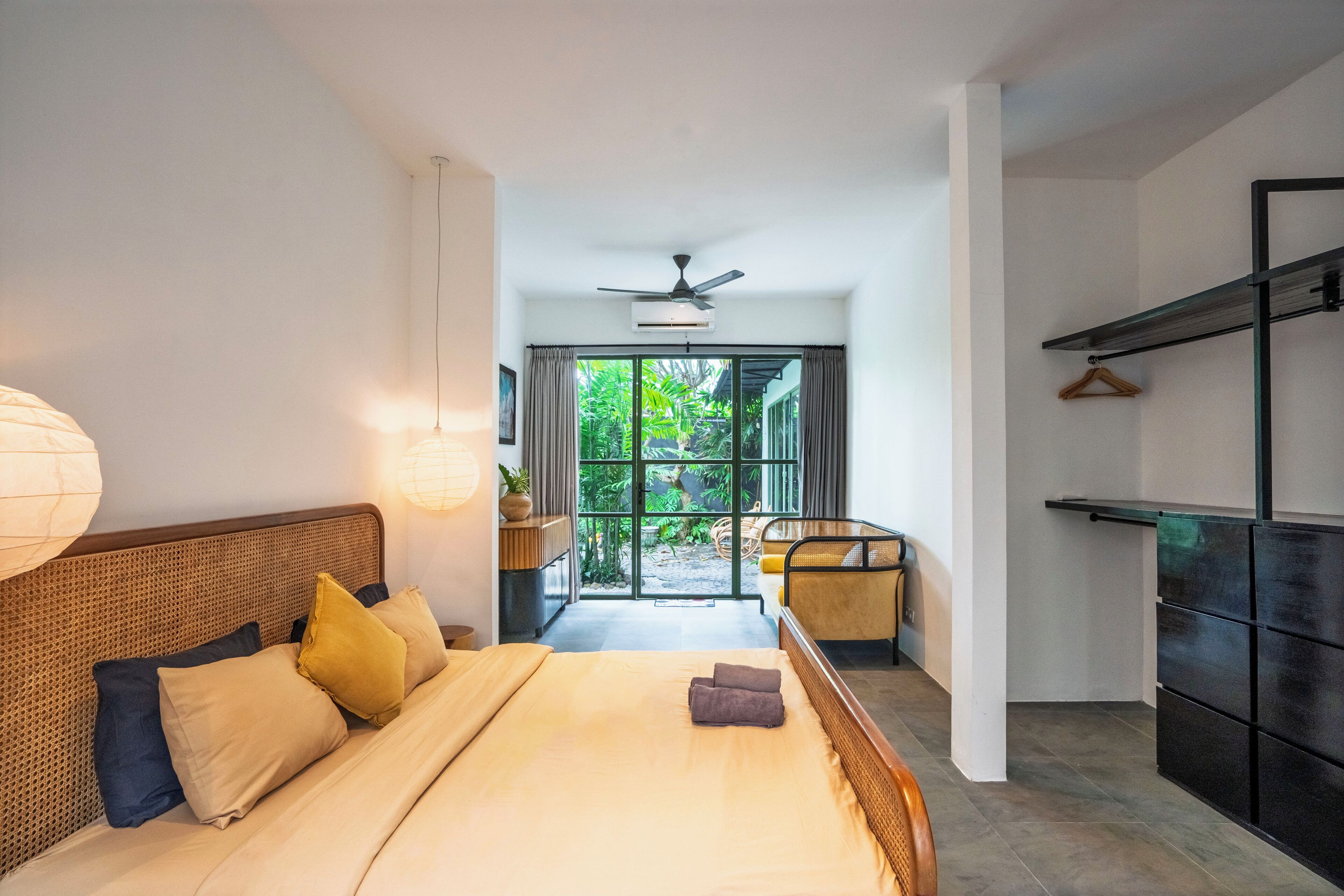 A hotel room with a bed, bedside lamps, a ceiling fan, and a view of the outdoors.