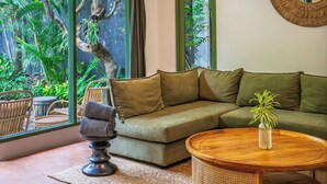 A cozy living room with a green sofa, a round coffee table, and a large window offering a view of lush greenery outside. - Veronica Villa by Betterplace (Canggu)