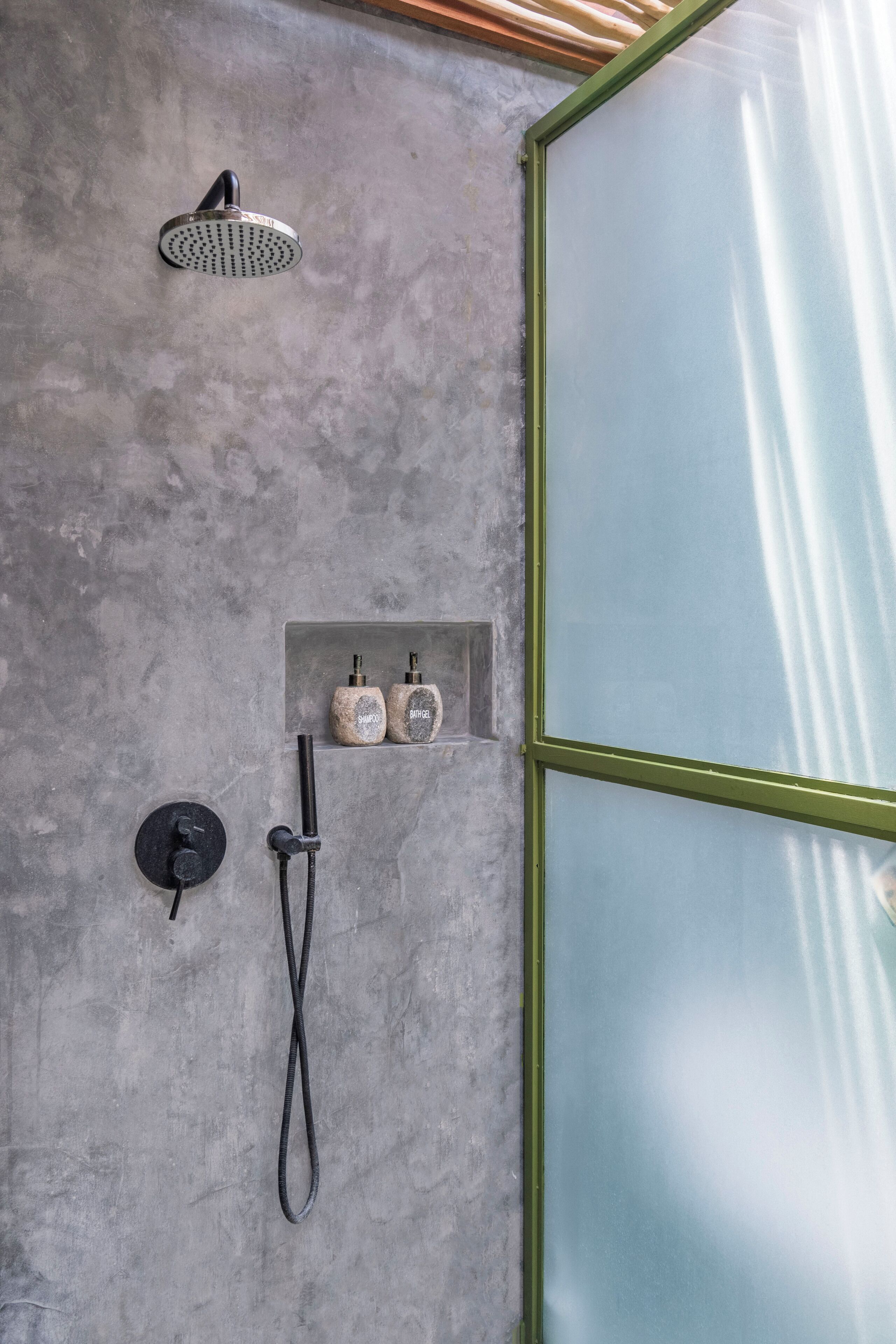 A shower with a handheld showerhead and a handheld shower attachment, a soap dish with two bottles, and a glass-enclosed shower area.