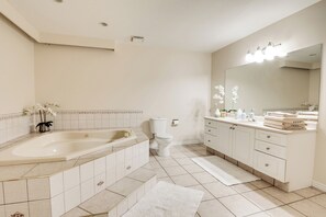 A modern bathroom with a large bathtub, a toilet, and a vanity with a mirror.