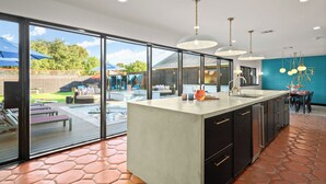 A modern kitchen with a large island, large windows, and a view of a pool and outdoor seating area. - Most EPIC Austin Experience! Sleeps 14 + heated Pool + Spa + Cabanas + Speakeasy (Austin)