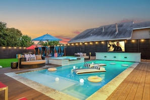 A backyard with a swimming pool, lounge area, and a bar.