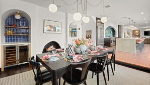 A modern dining area with a central table set for six, surrounded by black chairs. There is a kitchen area with a large island and bar seating. - Most EPIC Austin Experience! Sleeps 14 + heated Pool + Spa + Cabanas + Speakeasy (Austin)