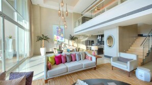 A spacious living area with a sofa, armchairs, and a coffee table. There are potted plants, a painting on the wall, and a staircase leading to an upper level. - Grand Luxxe 2 Bedroom Loft Residences 5 Diamonds all Platinum Access  (Nuevo Vallarta)