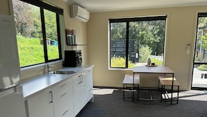 A modern kitchen with white cabinets, a stainless steel sink, and a black countertop. There is a window providing a view of greenery outside. - Nature on your door step (Waitati)