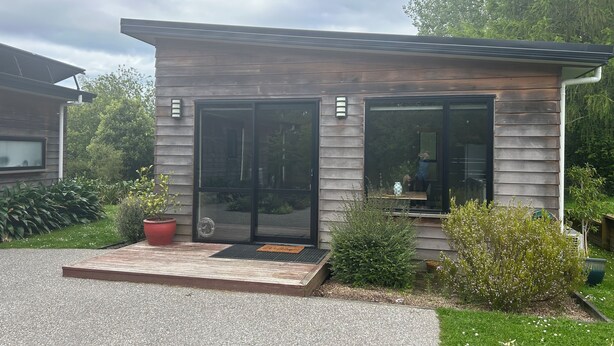 A modern house with large sliding glass doors, a small porch, and a well-maintained garden. - Nature on your door step (Waitati)