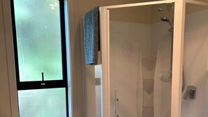 A modern bathroom with a glass-enclosed shower, a white sink, and a window. - Nature on your door step (Waitati)