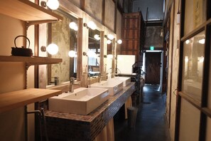 A long, narrow bathroom with three sinks, wooden shelves, and multiple mirrors. - lulu - Hostel (Kyoto)