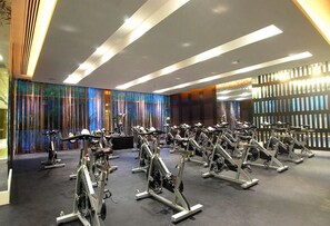 Uma academia com bicicletas ergométricas organizadas em fileiras, design moderno no teto e parede colorida com linhas verticais.