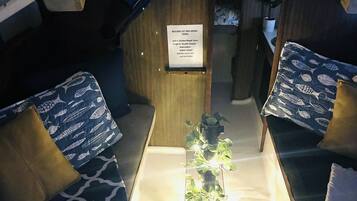 Un espace intérieur compact avec une table centrale, deux coins salon agrémentés de coussins à motifs, une petite plante en pot et un panneau indiquant des excursions en kayak.