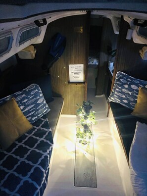 Un interior compacto con una mesa central, dos zonas de estar con cojines estampados, una pequeña planta en maceta y un cartel que ofrece tours en kayak.