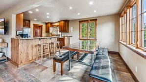 A spacious kitchen with wooden cabinets, a central island with stools, and a large window providing a view of greenery. - Breckenridge Escape with Hot Tub & Mountain Views (Breckenridge)