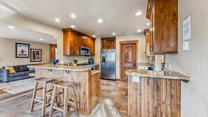 A modern kitchen with wooden cabinetry, a central island with stools, a built-in microwave, and a stainless steel refrigerator. - Breckenridge Escape with Hot Tub & Mountain Views (Breckenridge)