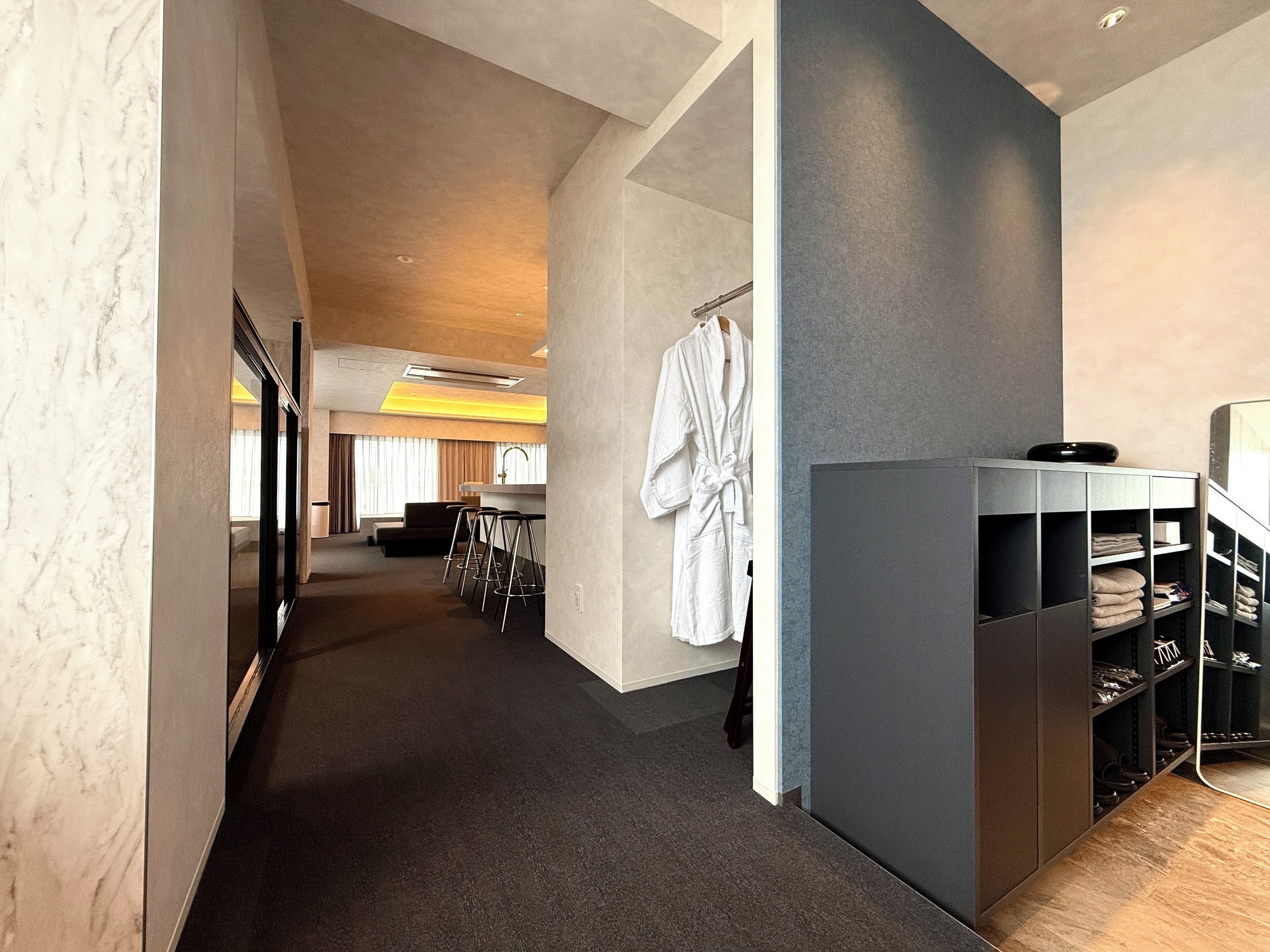 Un corredor de hotel moderno con una zona de estar, una bata colgada y un mueble para guardar zapatos.