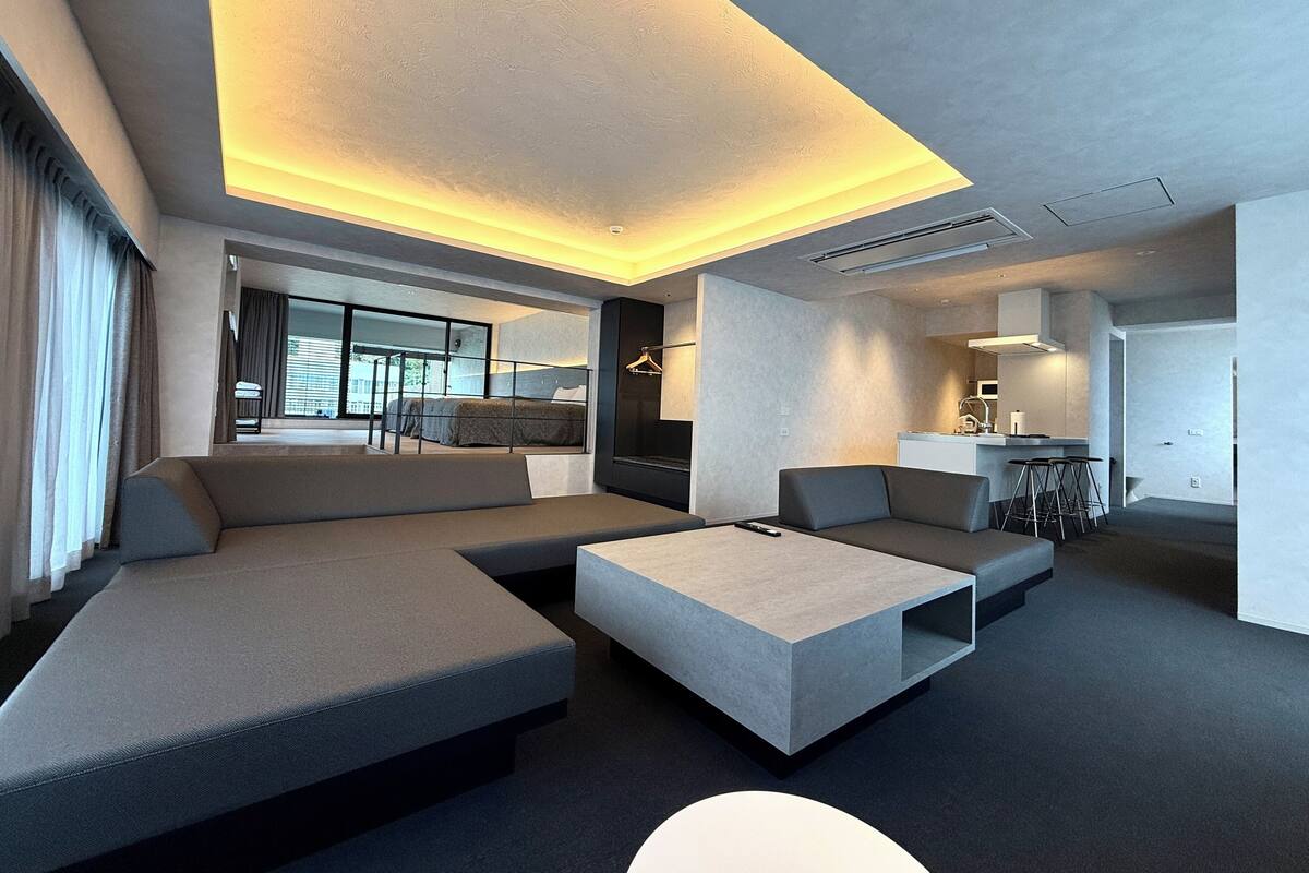 A modern living room with a sectional sofa, a coffee table, and a kitchen area in the background.