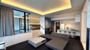 A modern living room with a large sectional sofa, a glass wall, and a kitchen area with bar stools. - DOG HOTEL SHIRAHAMA (Shirahama)