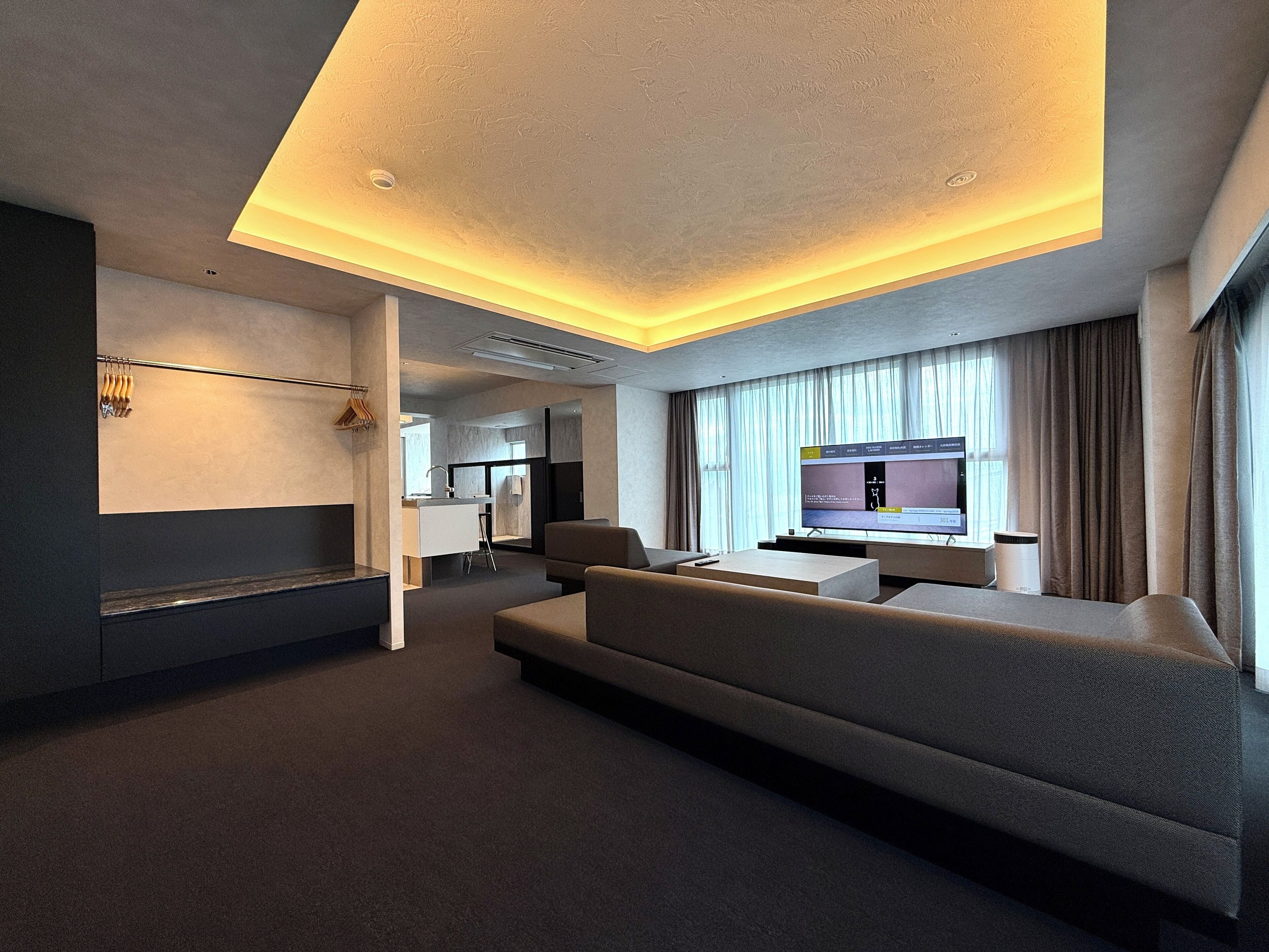A modern hotel room with a large sofa, a flat-screen TV, and a minimalist design.