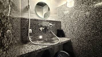A modern bathroom with a granite countertop, a handheld showerhead, a sink, and a mirror.