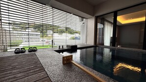 A modern indoor pool area with a wooden deck, a small pool, and a view of a cityscape through large windows. - DOG HOTEL SHIRAHAMA (Shirahama)