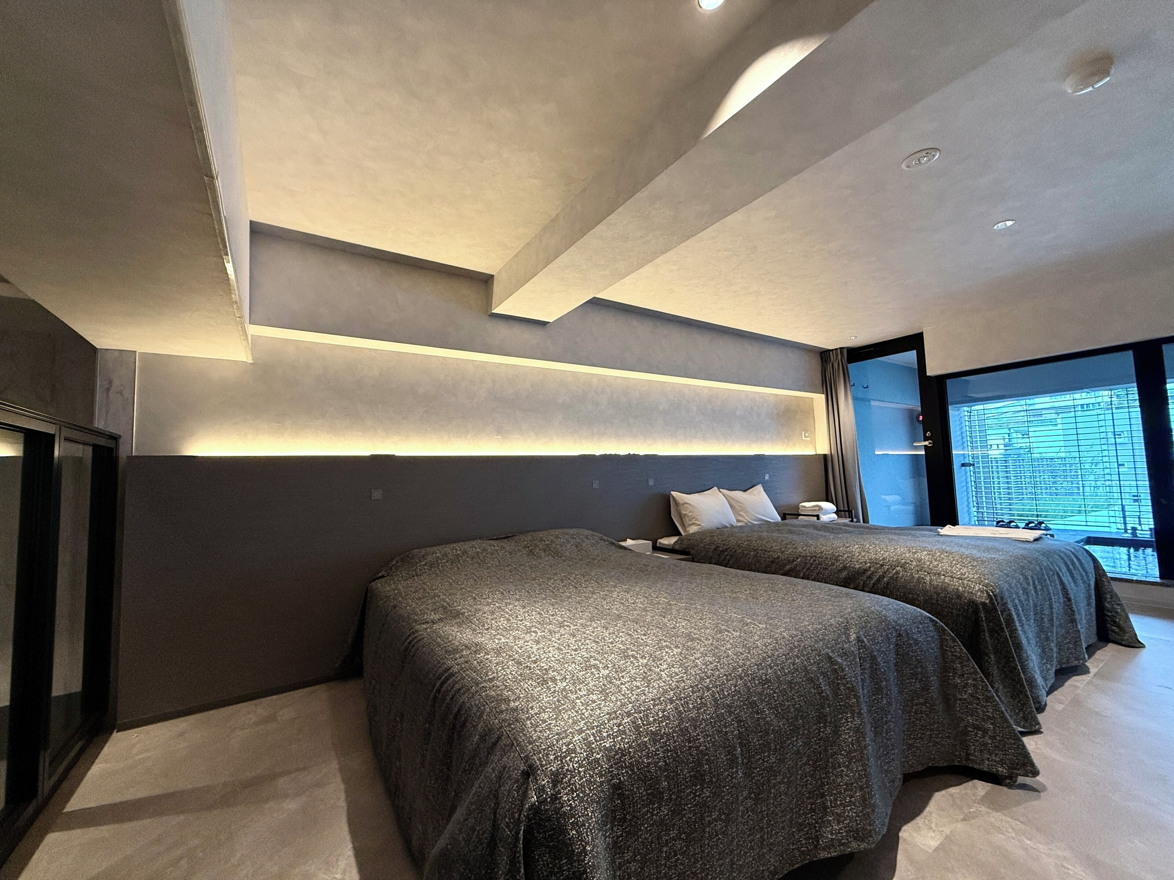 Una habitación de hotel moderna con dos camas, un ventanal grande y un diseño minimalista.