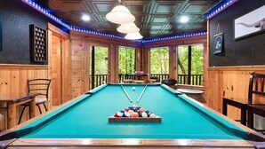 Une table de billard avec des billes, des murs en bois et un plafond éclairé de lumières bleues.