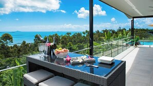 A balcony with a glass table, seating, and a view of the ocean.