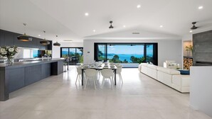 A modern kitchen with a dining area, large windows, and a view of the sea.