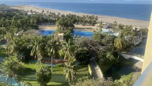 A resort with a swimming pool surrounded by palm trees and a view of the beach and ocean.