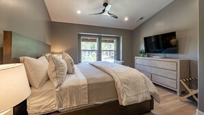 Une chambre à coucher avec un lit, une télévision, un ventilateur de plafond et une fenêtre donnant sur des arbres.