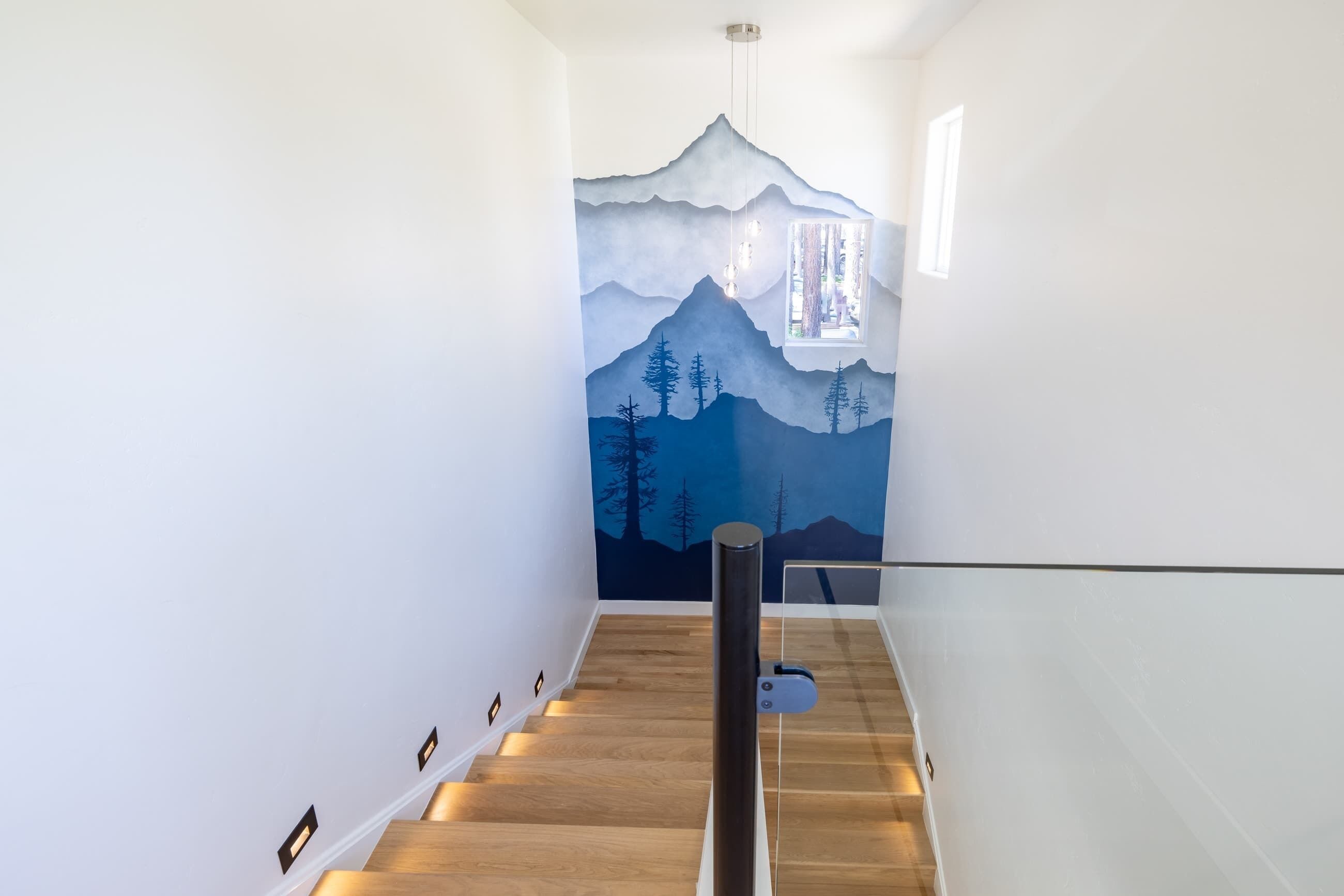 A staircase with a wooden finish and a wall mural depicting a mountain landscape.