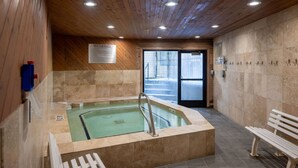 Ein Whirlpoolbereich mit Holzboden, gefliesten Wänden und einer Sitzbank.