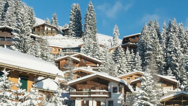 Ein schneebedecktes Chalet mit mehreren Holzhäusern, umgeben von hohen Nadelbäumen.