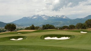 Ein Golfplatz mit Bunkern, Bäumen und Bergen im Hintergrund.
