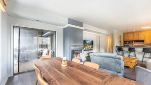 A modern living room with a wooden dining table, grey sofa, and a fireplace.