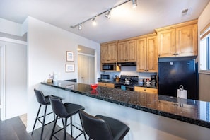 Eine moderne Küche mit Granit Arbeitsplatte, Holzschränken, einem schwarzen Kühlschrank und einer Mikrowelle.
