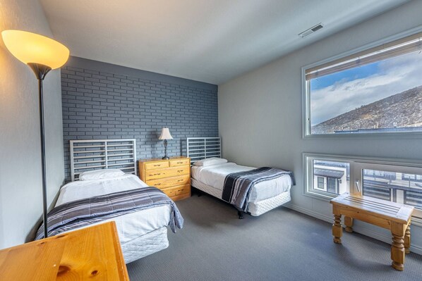 Un dormitorio con dos camas, un aparador, una lámpara y una ventana con vistas a una colina.