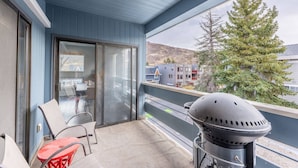 A balcony with a grill, chairs, and a view of buildings and trees.
