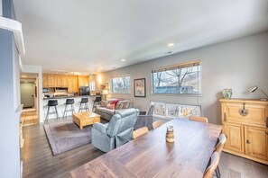 A modern kitchen with bar stools, a dining table, and a view through large windows.